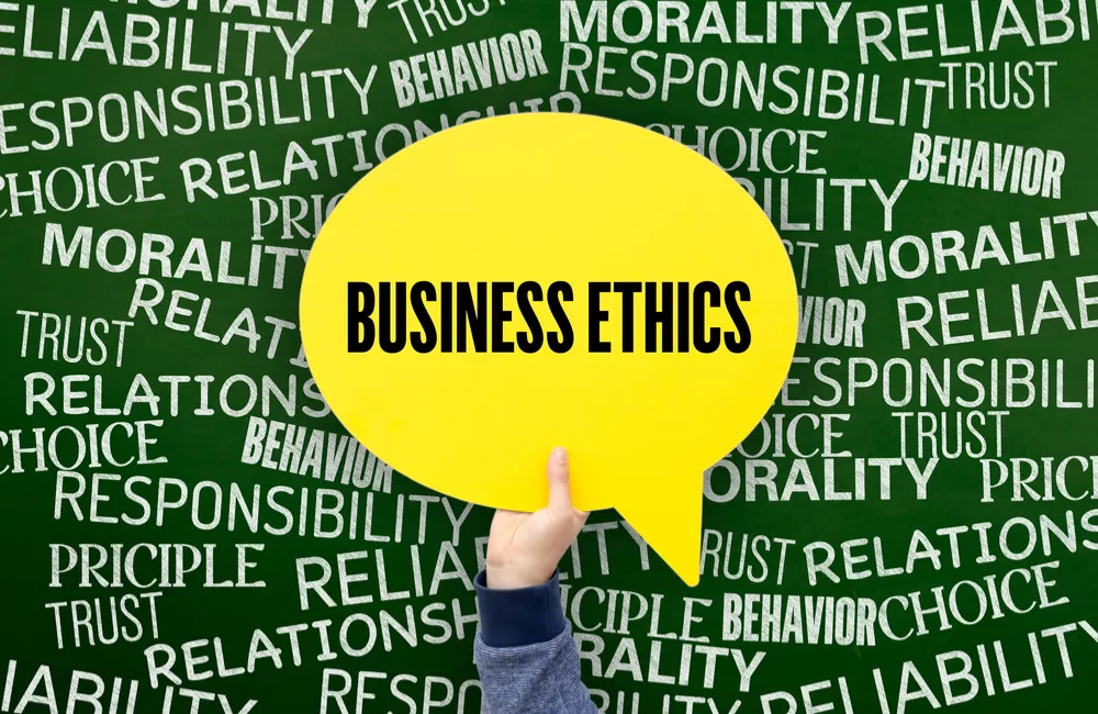 A hand holds up a yellow speech bubble with the words "Business Ethics" against a background of ethics-related words.