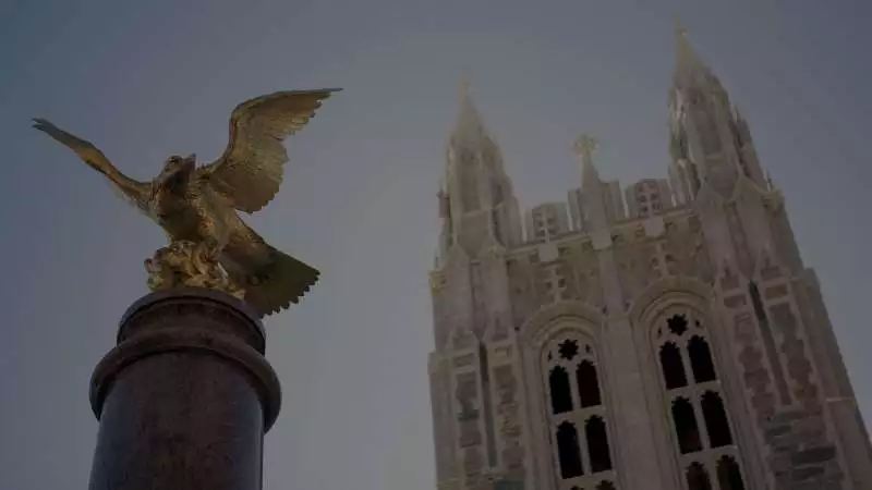 A golden eagle on top of a pedestal in front of one of Boston College's buildings.